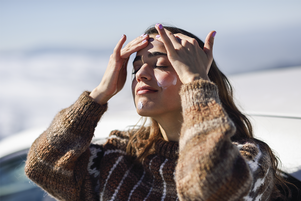 Mujer aplicándose protector solar en invierno mientras disfruta de un día soleado al aire libre.